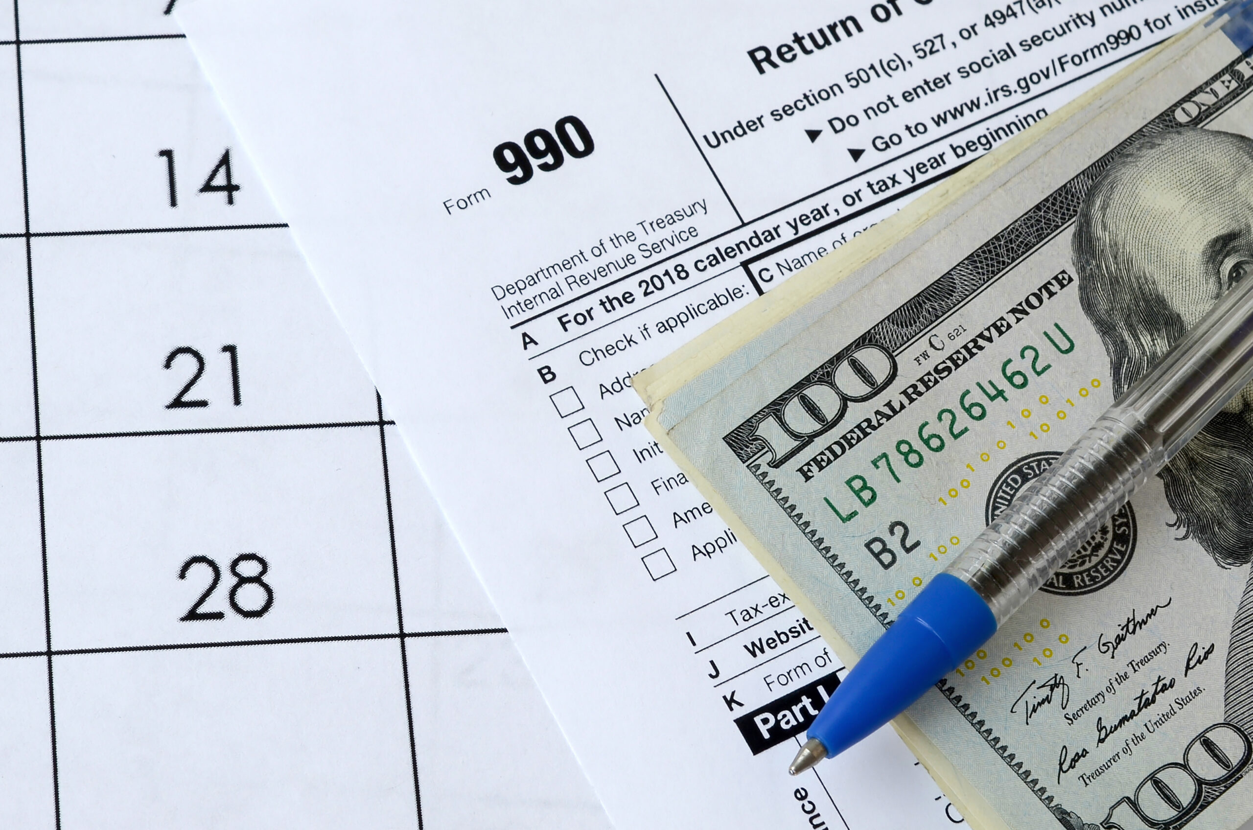 Form 990 Return of organization exempt from income tax and blue pen with dollar bills lies on office calendar. Internal revenue service tax form